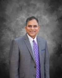 Dr. Shekar wearing a grey suit and purple tie smiling