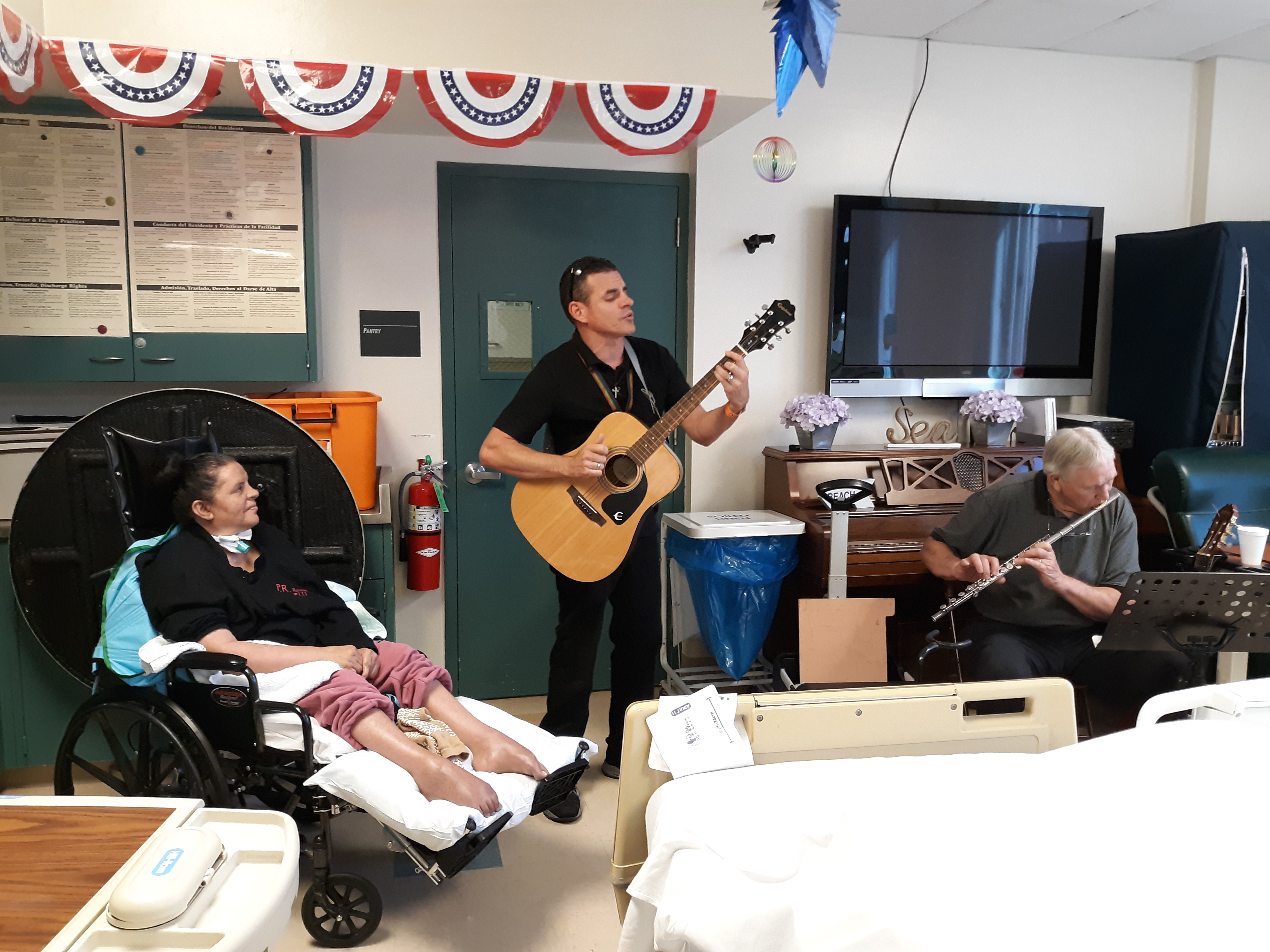 SVMC DPSNF Activities Area - patient listening to son play guitar and hospital volunteer play wind instrument 